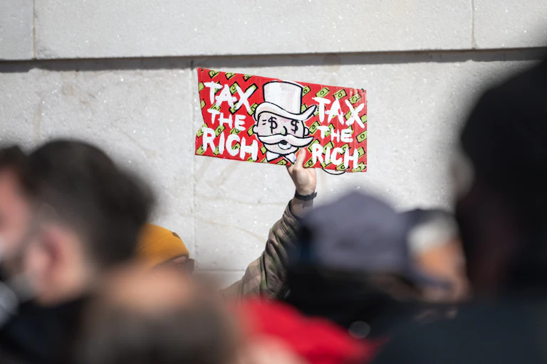 Manifestant portant un panneau avec écrit "tax the rich".