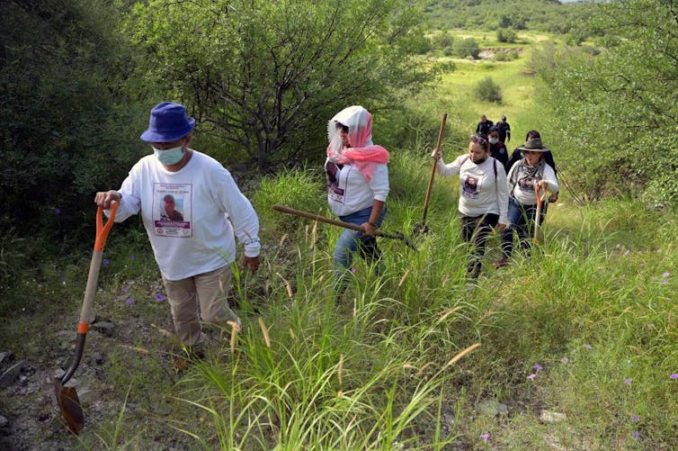 A group of women wearing white, long-sleeved shirts hike up a hill.