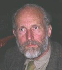 A man wearing a suit with gray hair and a beard.