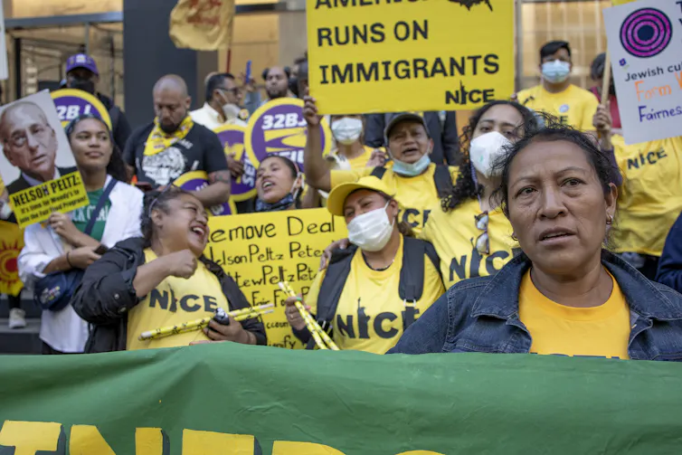 A group of women and men wearing yellow shirts hold signs, one of which says, 'America runs on immigrants.'