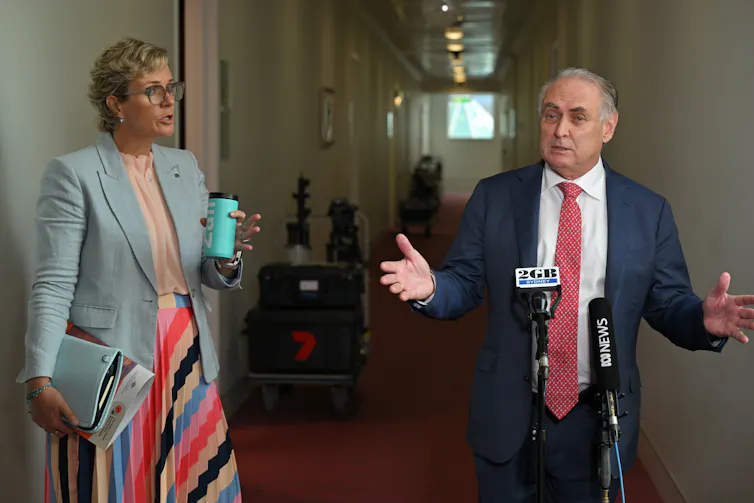 A womn wearing a colorful striped skirt confronts a man wearing a red tie who is talking to the media