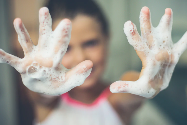 A little girl reaches toward the camera with her soapy hands.