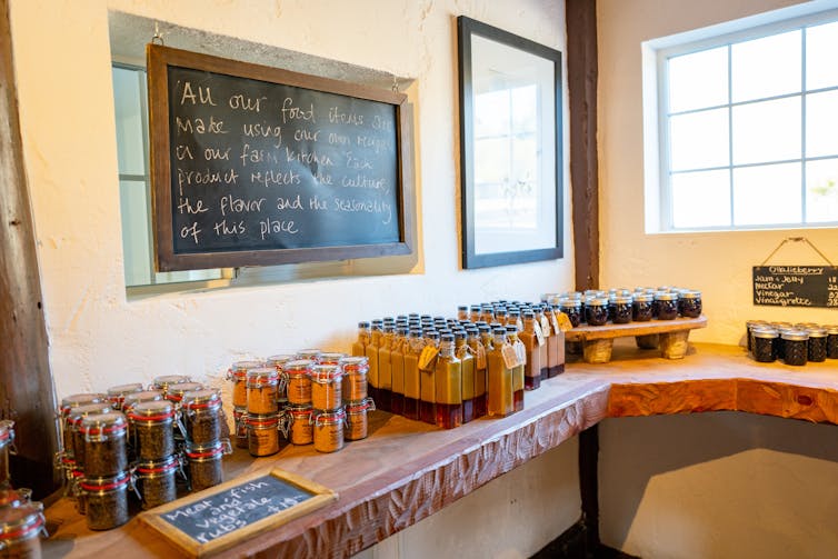 Meats and jams fill tables at a farm store. A hand-written sign on a chalkboard says: 'All our food items are made using our own recipe in our farm kitchen, and the product reflects the culture, the flavor and the seasonality of this place.'