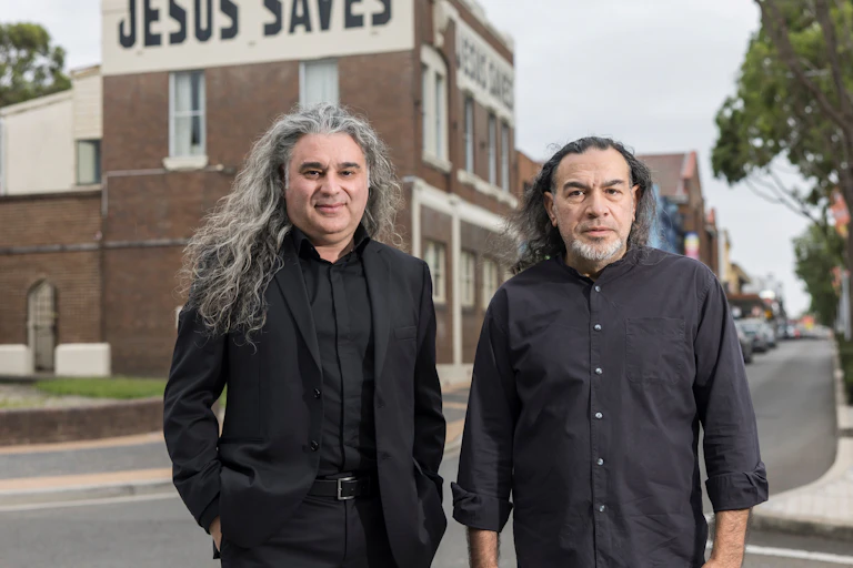 Two men in black pose for a photograph.