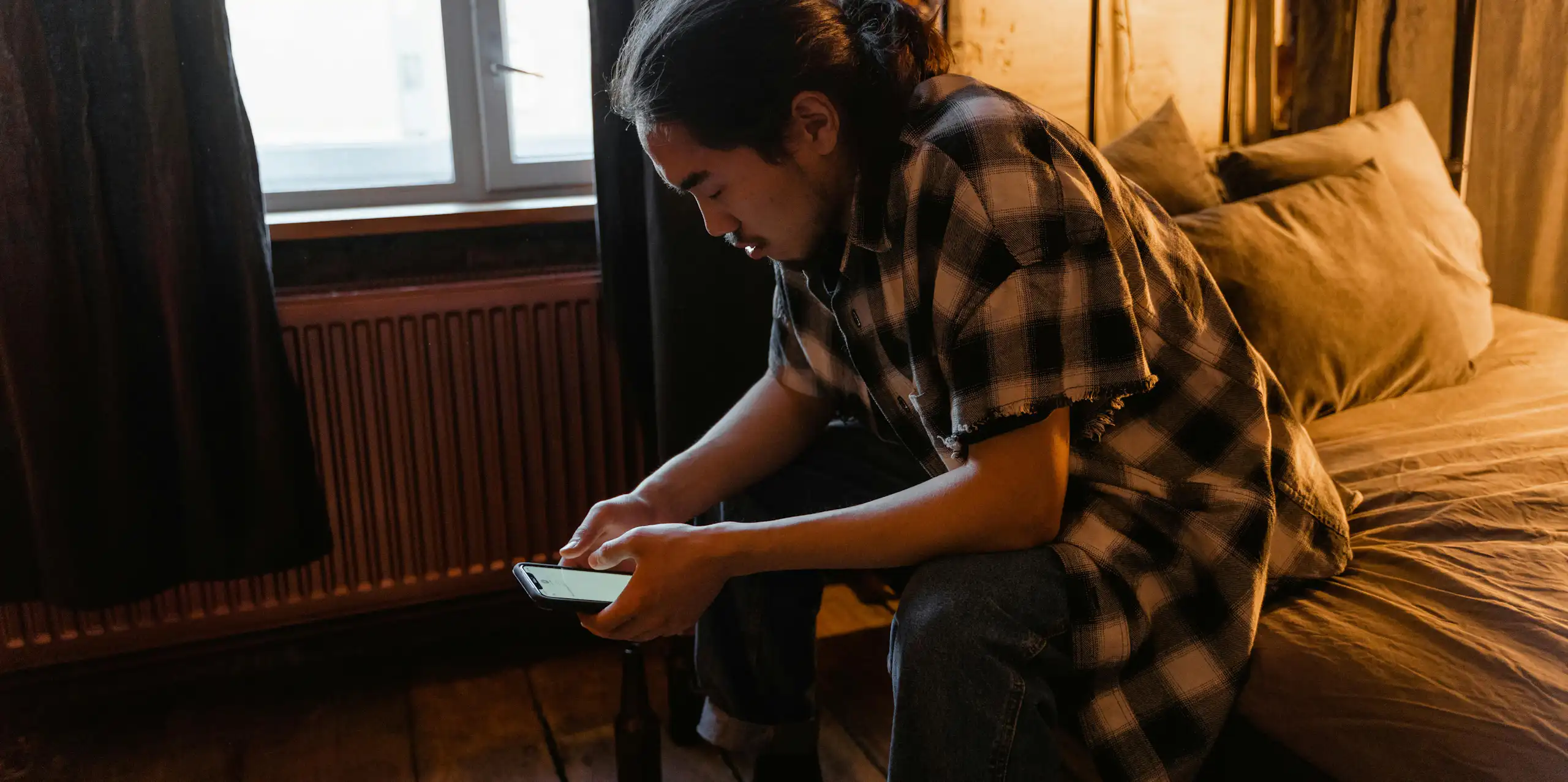 A man sitting on a bed looking at his phone.