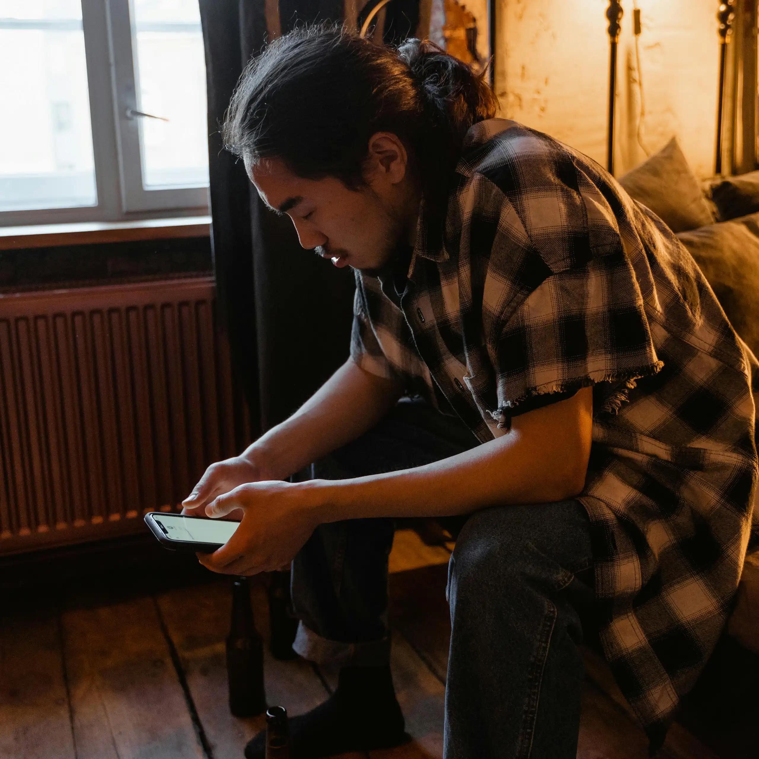 A man sitting on a bed looking at his phone.