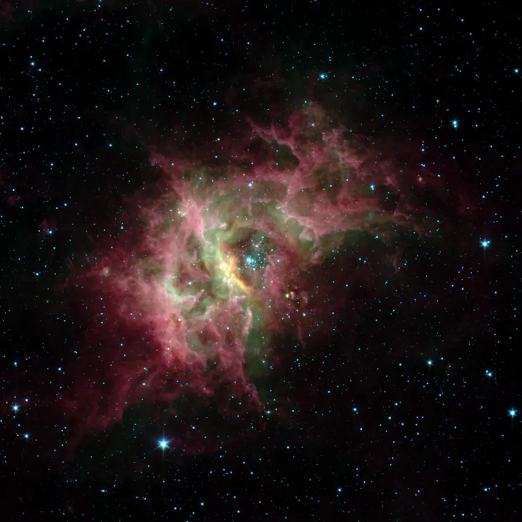 Cloud of pink and green dust surrounded by stars.