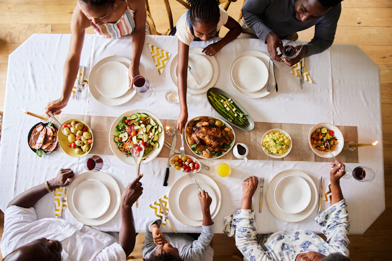 A wide overhead image of a multi-generational family tucking into various meat and vegetable dishes
