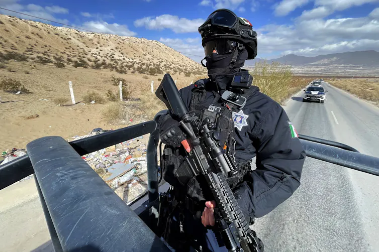 A member of Mexico's state police riding on the back of a vehicle patrolling the border with the US.
