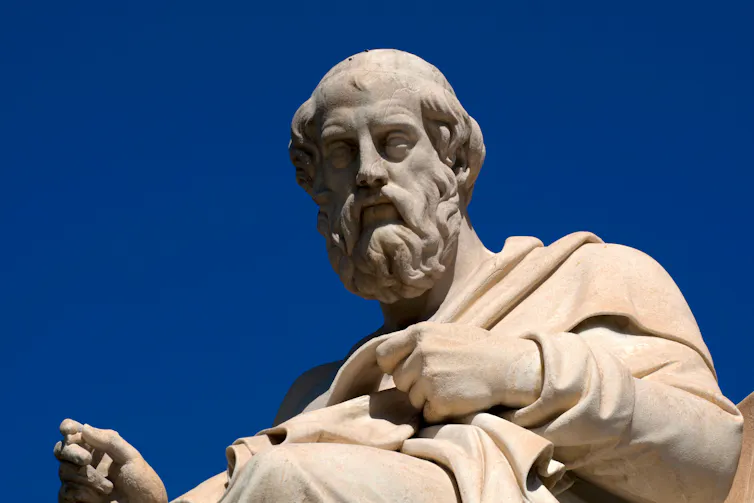A statue of Plato against a blue sky in Athens.