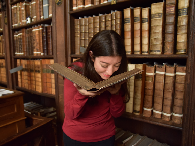 Cecilia Bembibre smelling an old book in a library