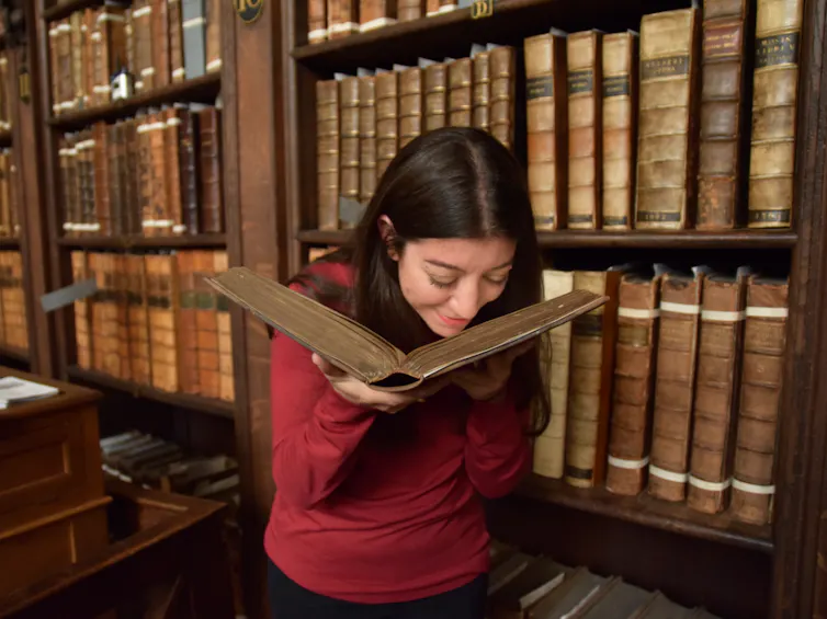 Cecilia Bembibre smelling an old book in a library