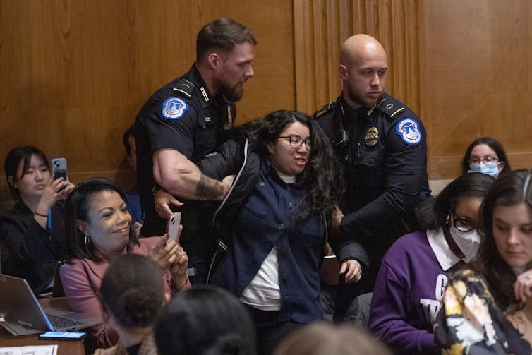A woman being detained by two police officers in a crowd of people.
