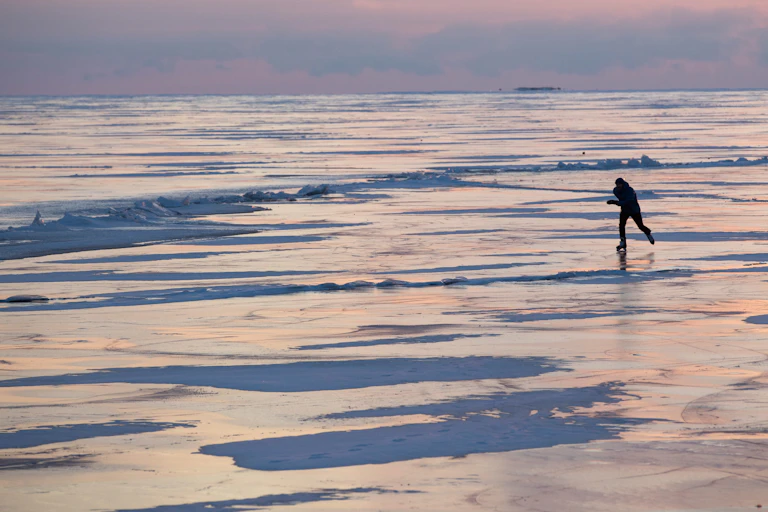 A person skates across Lake Ontario during the sunset.