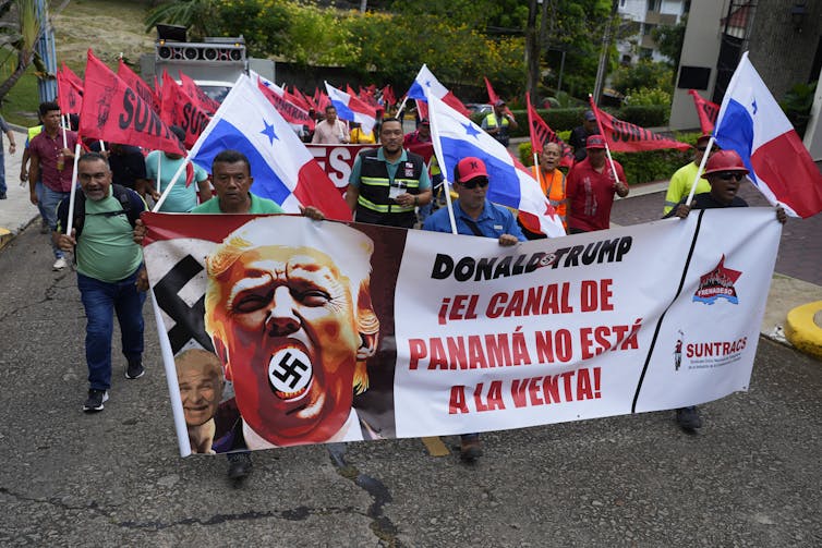 Group of people march holding signs saying the 'Panama Canal is not for sale' with a picture of Trump
