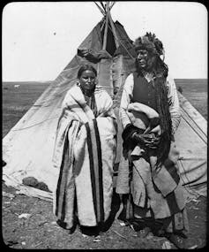 A woman and a man stand in front of a tipi