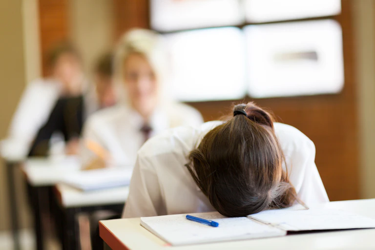 A girl puts her head on the desk in the classroom.