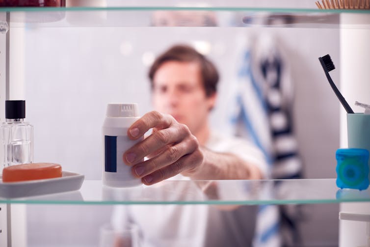 man taking pills from a bathroom cabinet