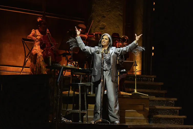 Anu in a silver suit, in front of the band.