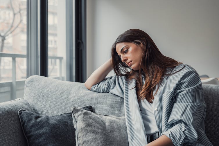A young woman sitting on a couch appears despondent.