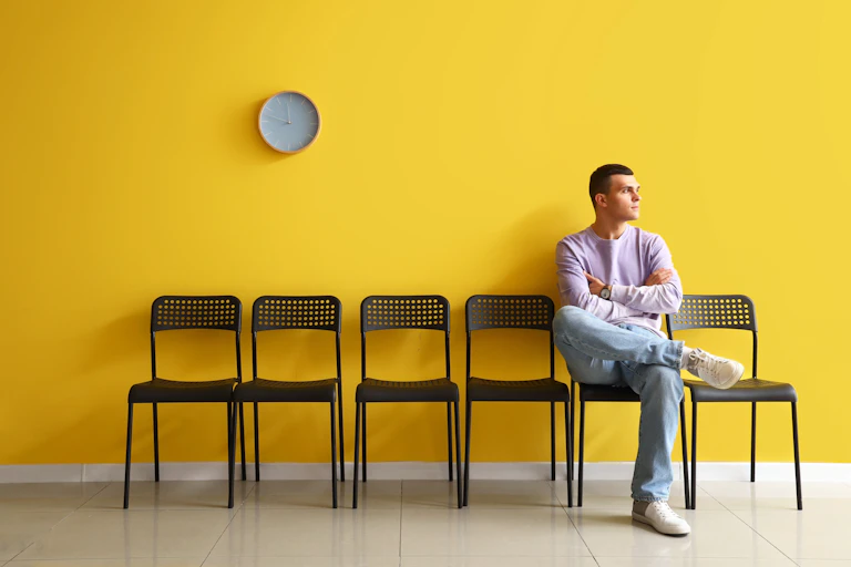 A man sitting in a waiting room with a yellow wall.