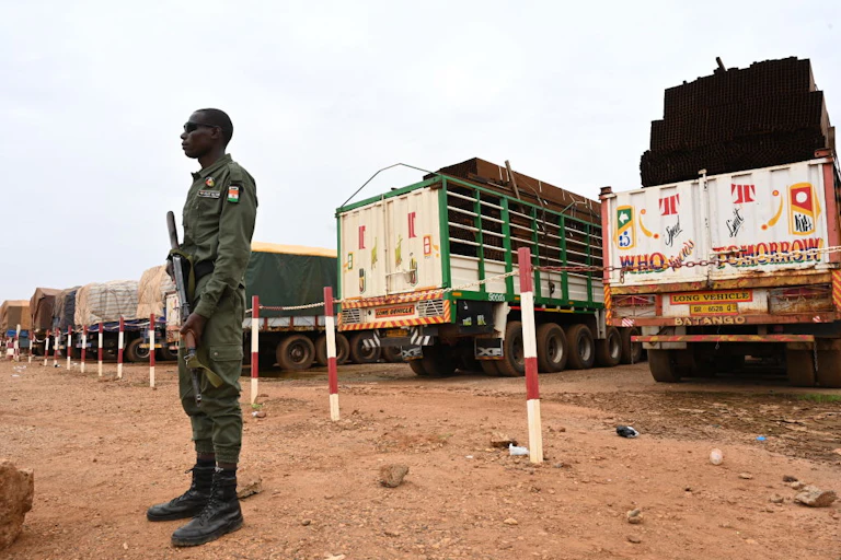 An armed police officer stands guard over trucks loaded with food.