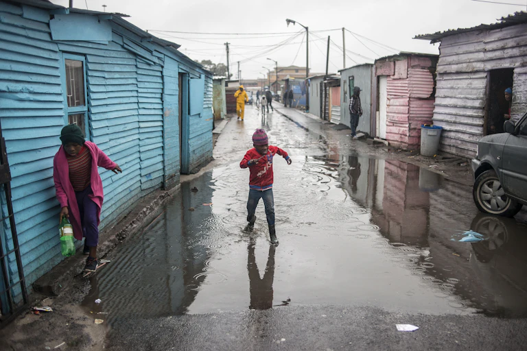 Young boys run through flood water blocking a street after heavy rainfalls in an informal settlement in Langa, Cape Town.