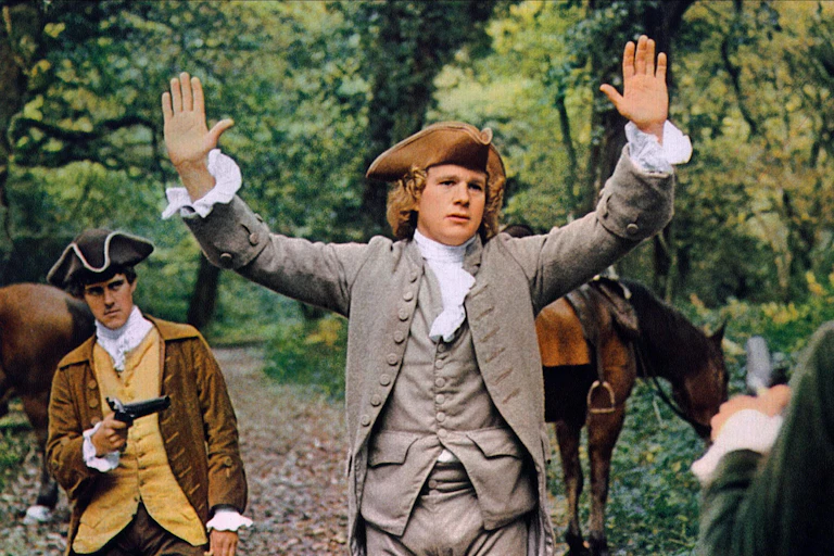Ryan O'Neal holds his hands up wearing an 1800s costume.