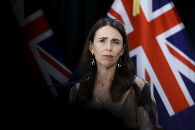 Jacinda Ardern standing in front of a New Zealand flag.