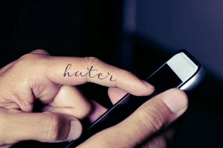 A finger with 'hater' written on it touching a phone.