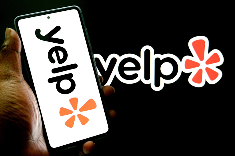In a photo illustration, the Yelp logo is seen displayed on a smartphone and in the background.