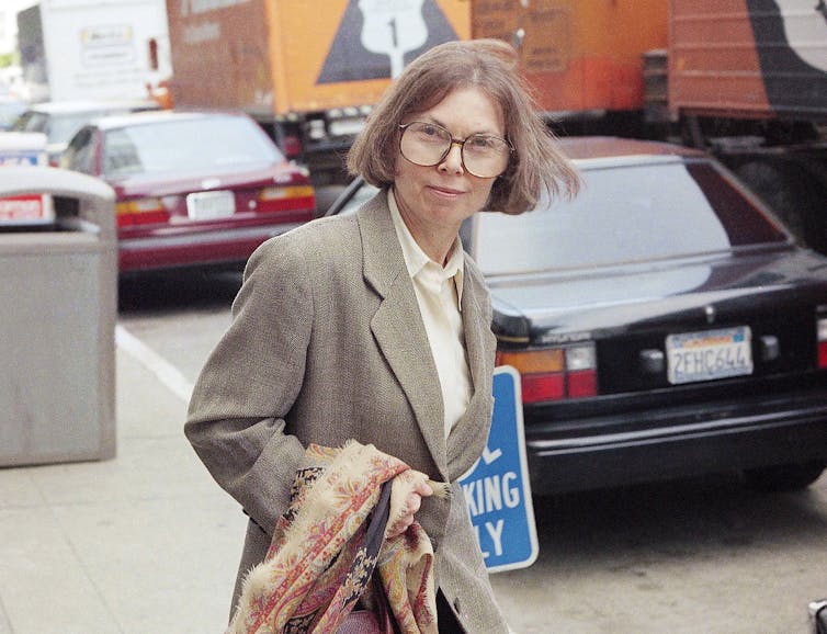 A woman with a brown bob and large, round spectacles (Janet Malcolm) leaving a courtroom.