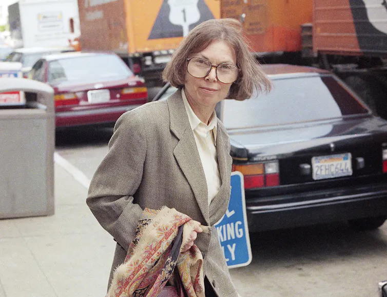 A woman with a brown bob and large, round spectacles (Janet Malcolm) leaving a courtroom.