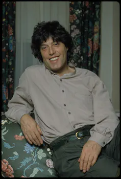 A dark-haired man sitting in a floral armchair.