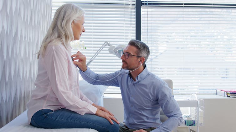 A male doctor uses a stethoscope on a female patient.