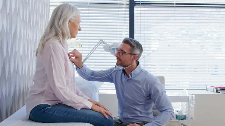 A male doctor uses a stethoscope on a female patient.