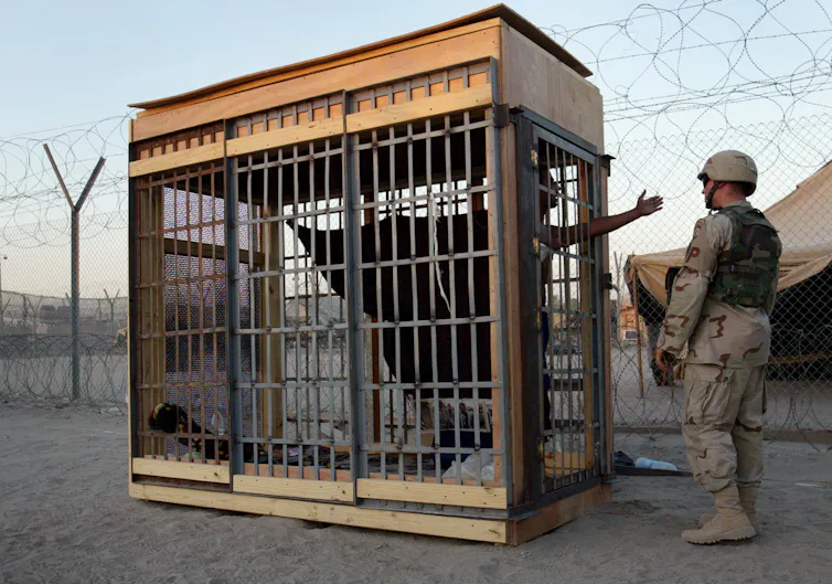 A prisoner in a cage reaches out to an American soldier.
