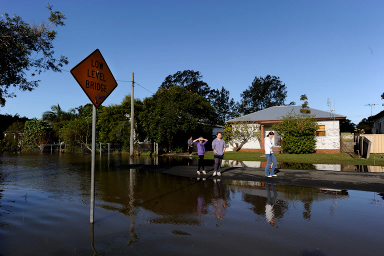 three people stand outside a flooded house