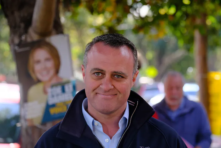 Former Liberal MP Tim Wilson standing in front of political corflutes.
