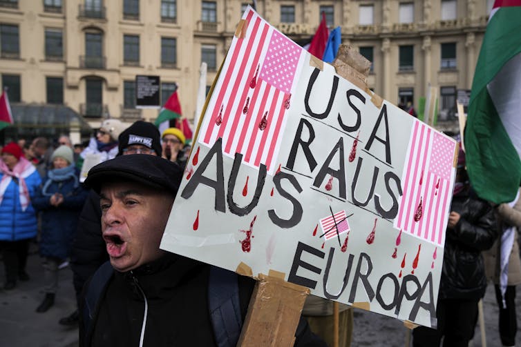 Man holds protest sign in crowded public square.