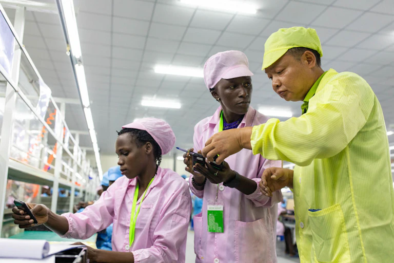 A man in yellow uniform showing two other workers dressed in pink uniform how to assemble a mobile phone
