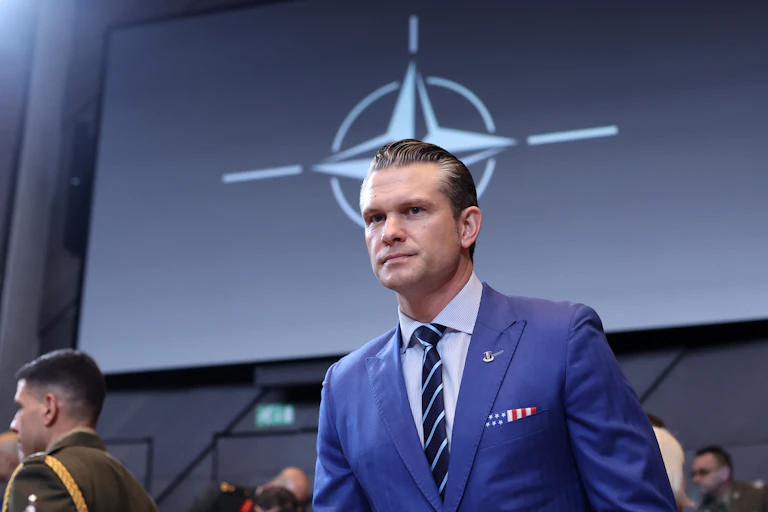 Pete Hegseth standing in a suit in front of the Nato logo.