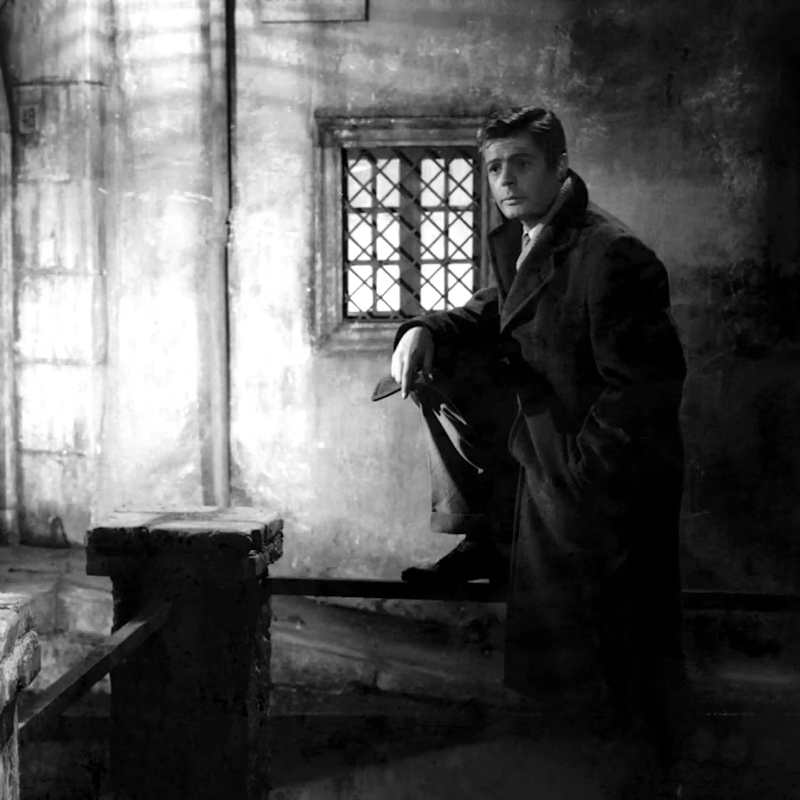 Un hombre mira a una mujer que está en primer plano desde el fondo de la habitación.