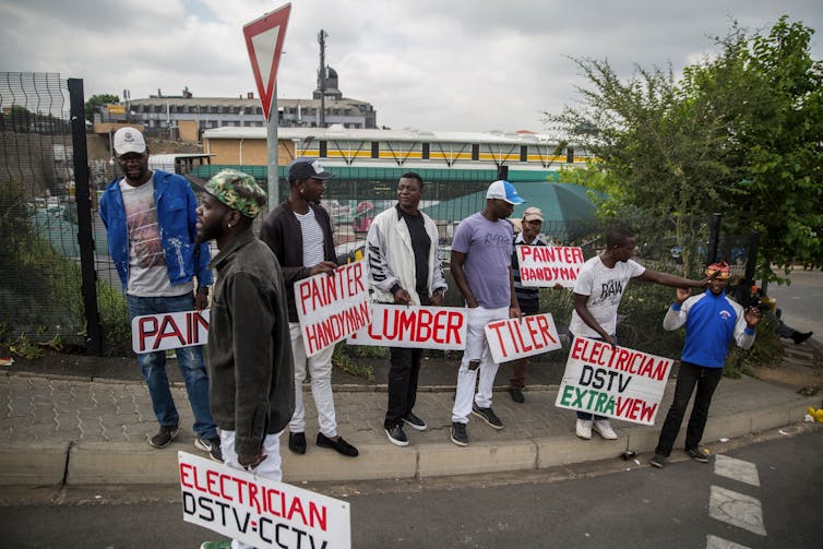 Unemployed builders, tilers, and plumbers hold signs advertising their skills on the side of the road in Johannesburg, South Africa.