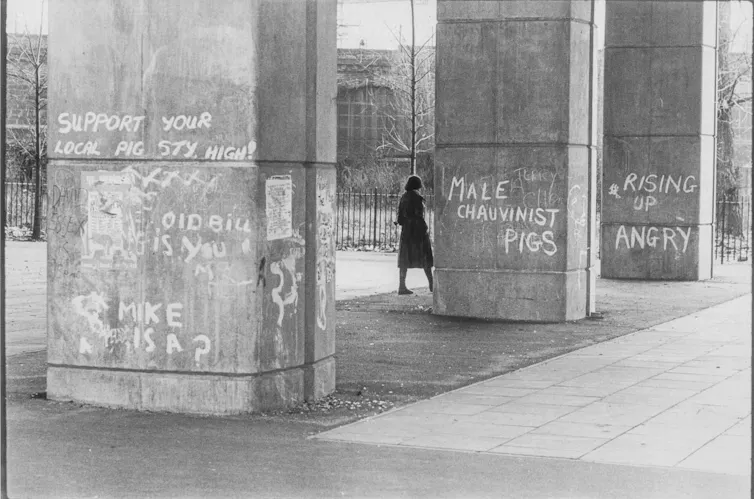 An image of a woman walking through the base of some brutalist architecture covered in graffiti.