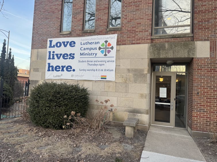 A brick building has a large sign that says 'Love lives here' and a glass door with a smaller white sign on it.
