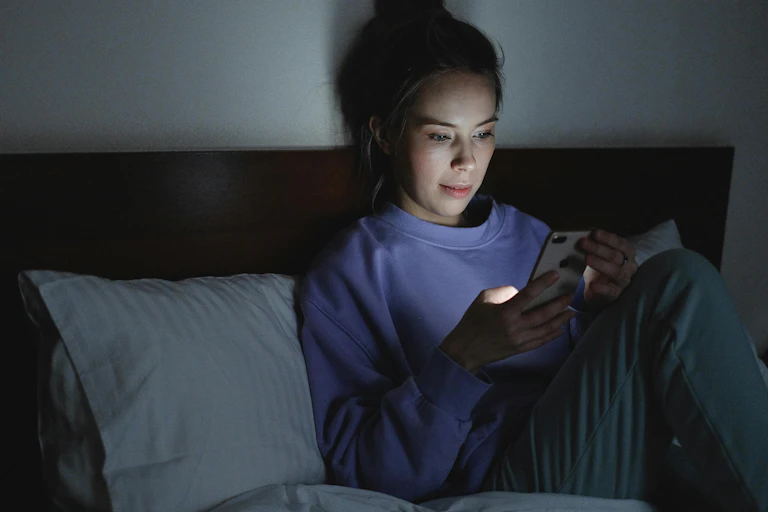 Woman sits in bed looking at her phone