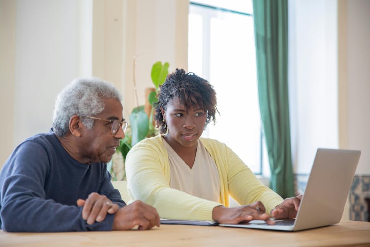 An African-Australian woman shows her older relative how to use ChatGPT