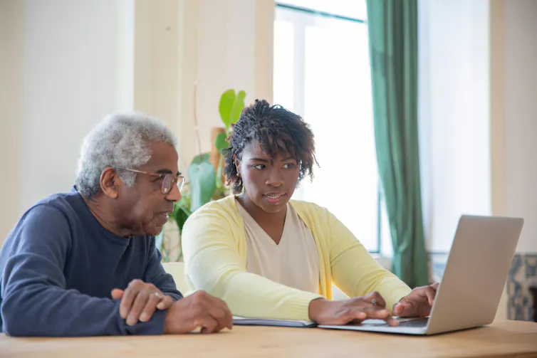 An African-Australian woman shows her older relative how to use ChatGPT