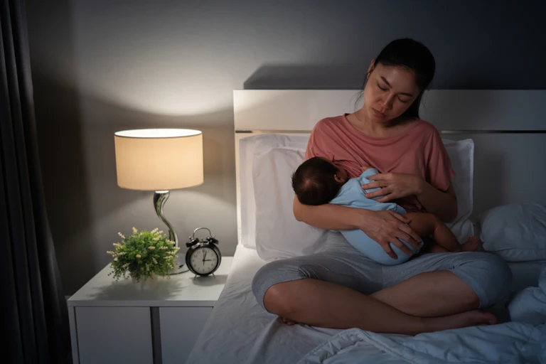 Tired mother breastfeeding baby at night